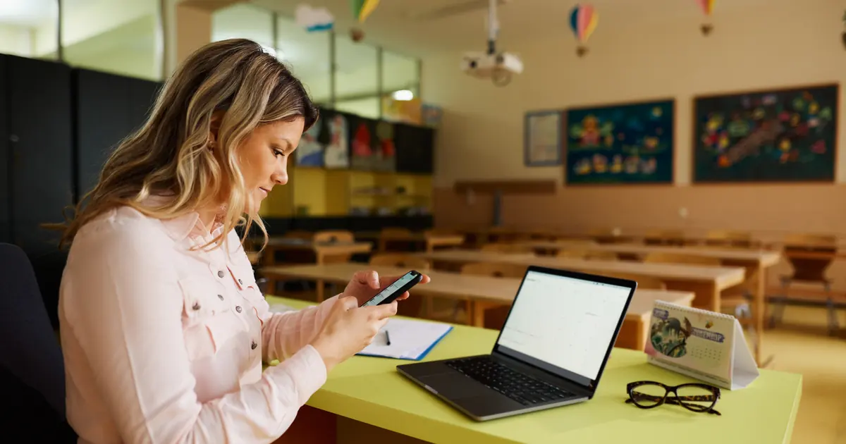 Illustrative photo of a woman reading a message on her phone in a classroom.