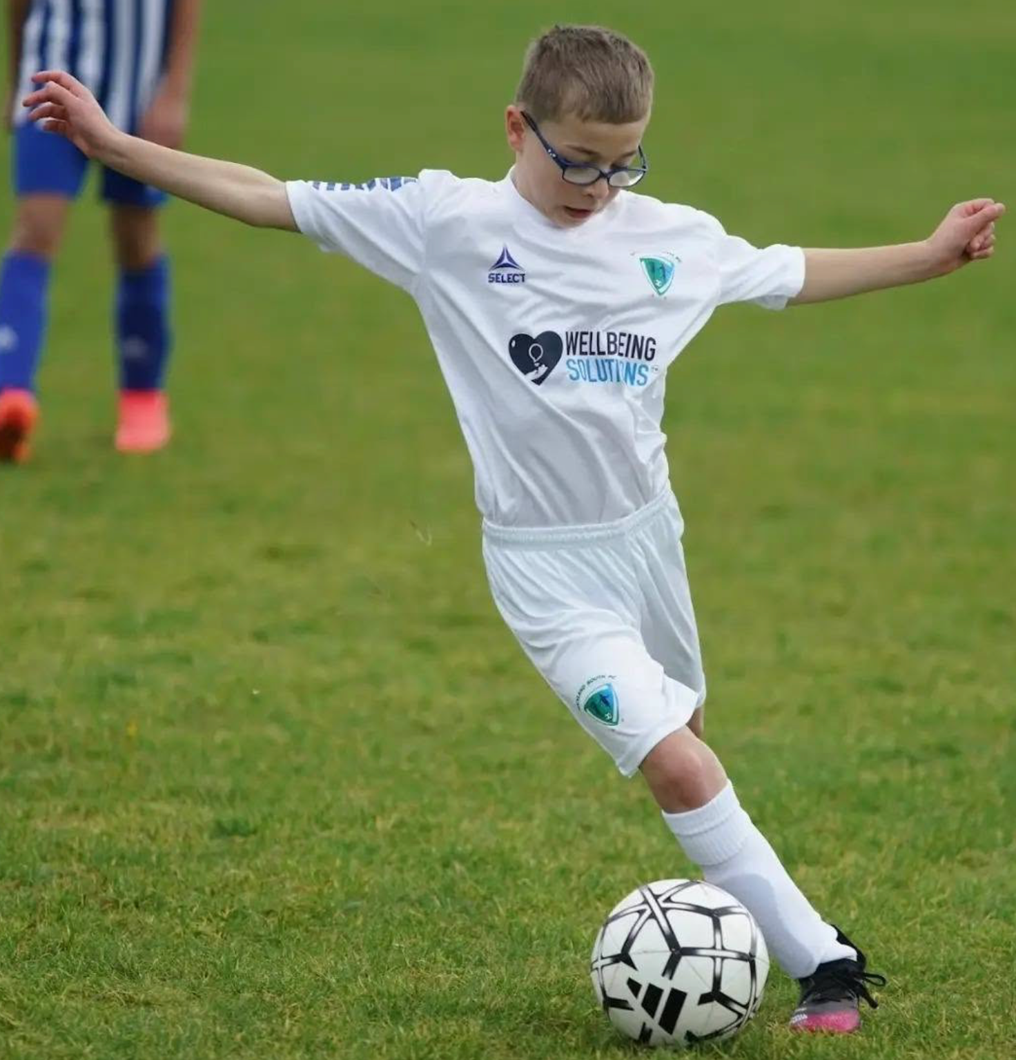 Young footballer playing with the ball in a white WellbeingSolutions-sponsored kit